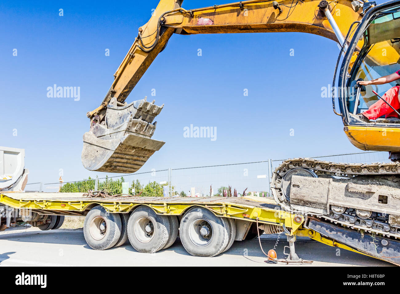 Schwere Bagger klettert es auf niedrige Plattform Anhänger über rückseitige Rampe, trägt zwei Eimer ineinander eingefügt. Stockfoto