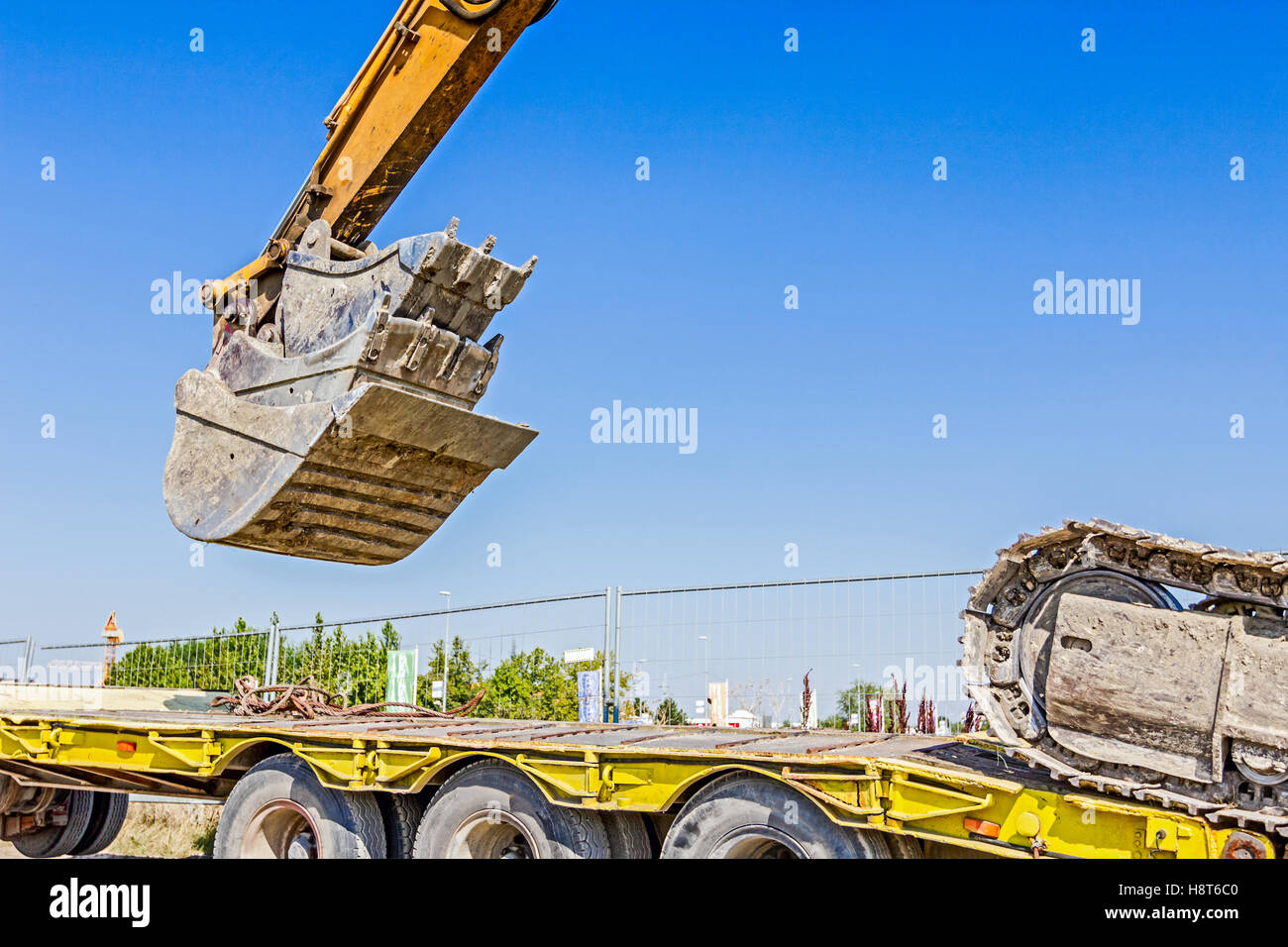 Schwere Bagger klettert es auf niedrige Plattform Anhänger über rückseitige Rampe, trägt zwei Eimer ineinander eingefügt. Stockfoto