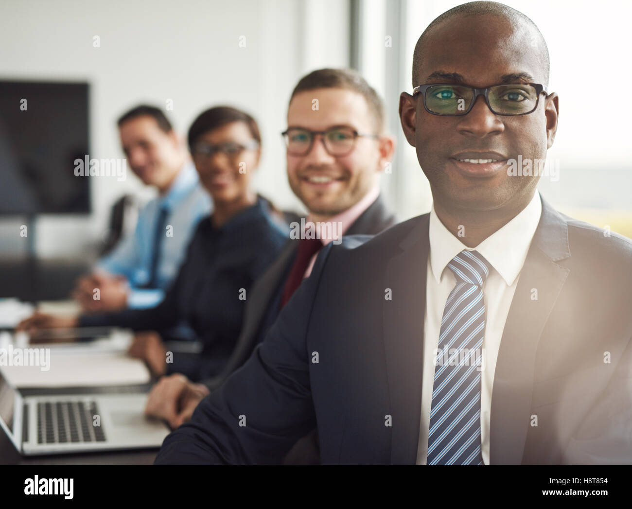 Freundlichen zuversichtlich afrikanischen Geschäftsmann in einem Management-Meeting mit einer Gruppe von Rassen Kollegen lächelnd in die Kamera Stockfoto