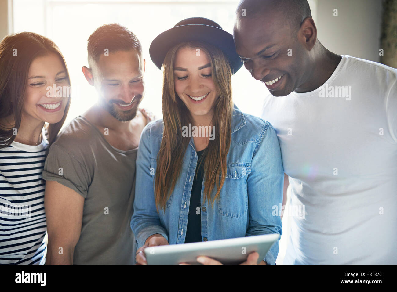 Heterogene Gruppe von vier erwachsenen Männern und Frauen lachen eng beieinander stehen, um einen Tabletcomputer Stockfoto