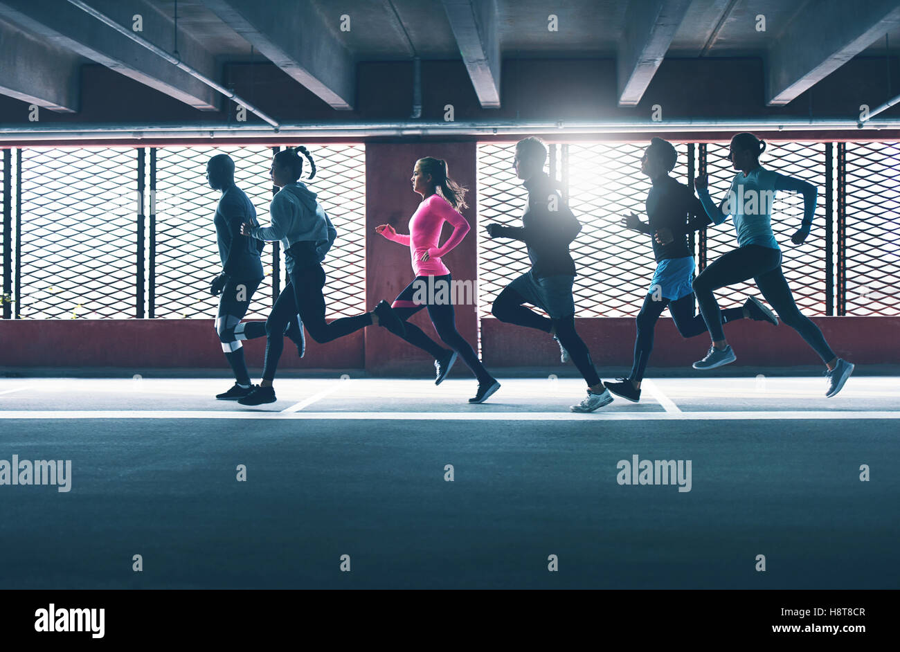 Gruppe von vielfältigen städtischen Läufer sprinten über den Rahmen in ein Parkhaus als sie Training Hintergrundbeleuchtung von der Sonne durch ein Gri Stockfoto