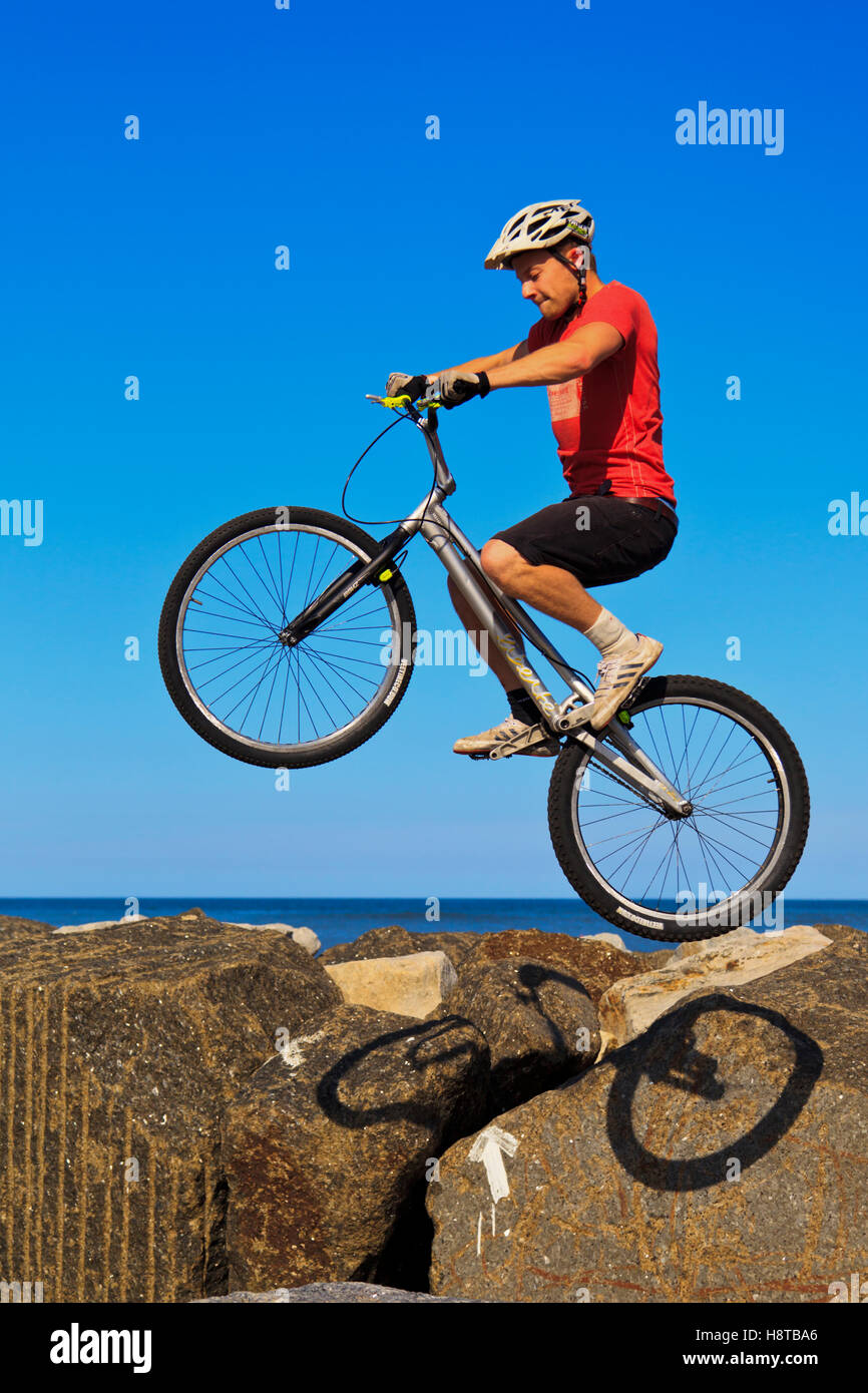 Mountainbiker, springen über Felsen auf der Hafenmauer in Staithes, North Yorkshire Stockfoto