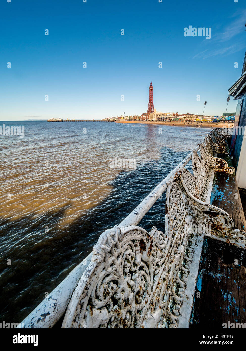 Traditionelle Gusseisen Sitze in einem Zustand des Verfalls am Pier mit Blackpool Tower in Ferne, Blackpool, Lancashire, UK. Stockfoto