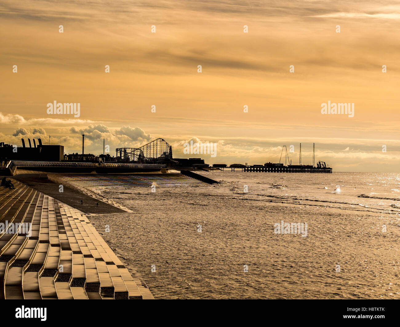 South Pier und Pleasure Beach Big Dipper mit Steinstufen Küstenschutzes und irische See im Vordergrund bei Sonnenuntergang, Blackpool, Lancash Stockfoto