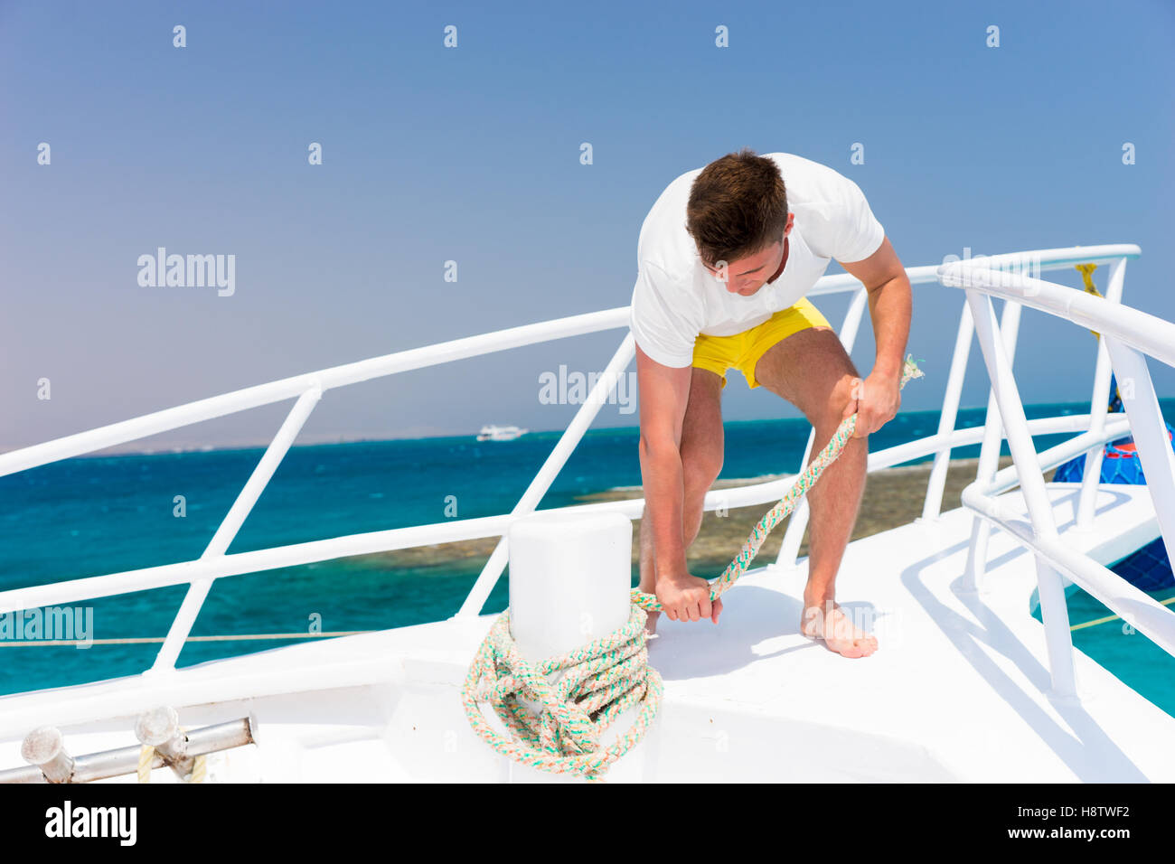 Schöner junger Mann behebt Seil auf Yacht an einem sonnigen Sommertag, schöne Meer im Hintergrund Stockfoto