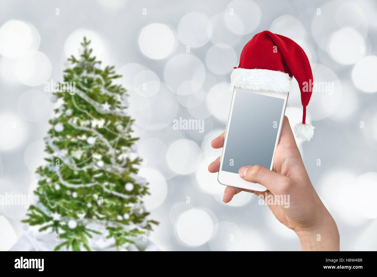 Hand, die eine Smartphone mit einem Santa Hut, Weihnachtsbaum und Bokeh Hintergrund Stockfoto