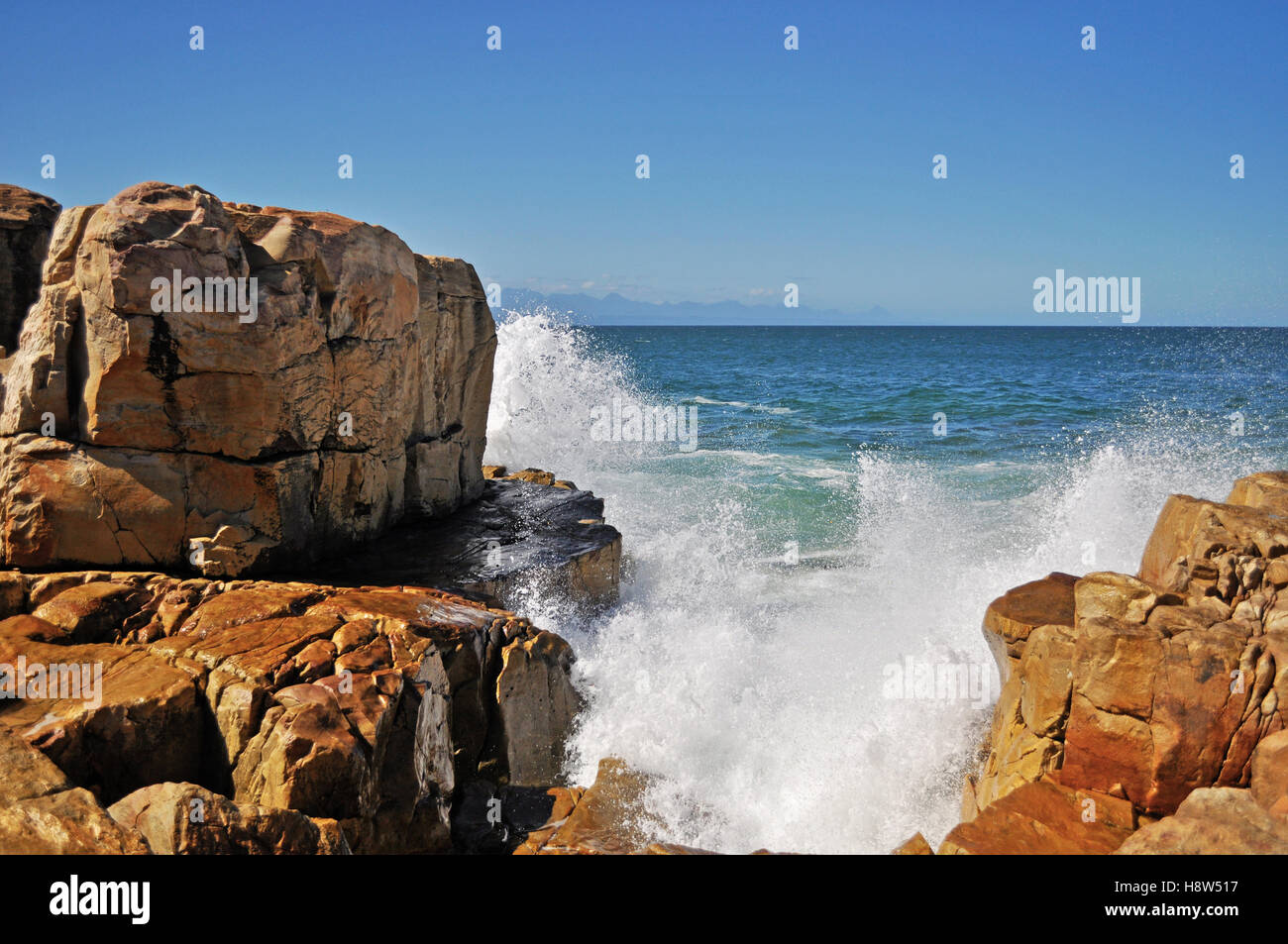 Südafrika: Brechen von Wellen auf dem roten Felsen am Strand von Plettenberg Bay, einer Stadt an der berühmten Garden Route. Stockfoto