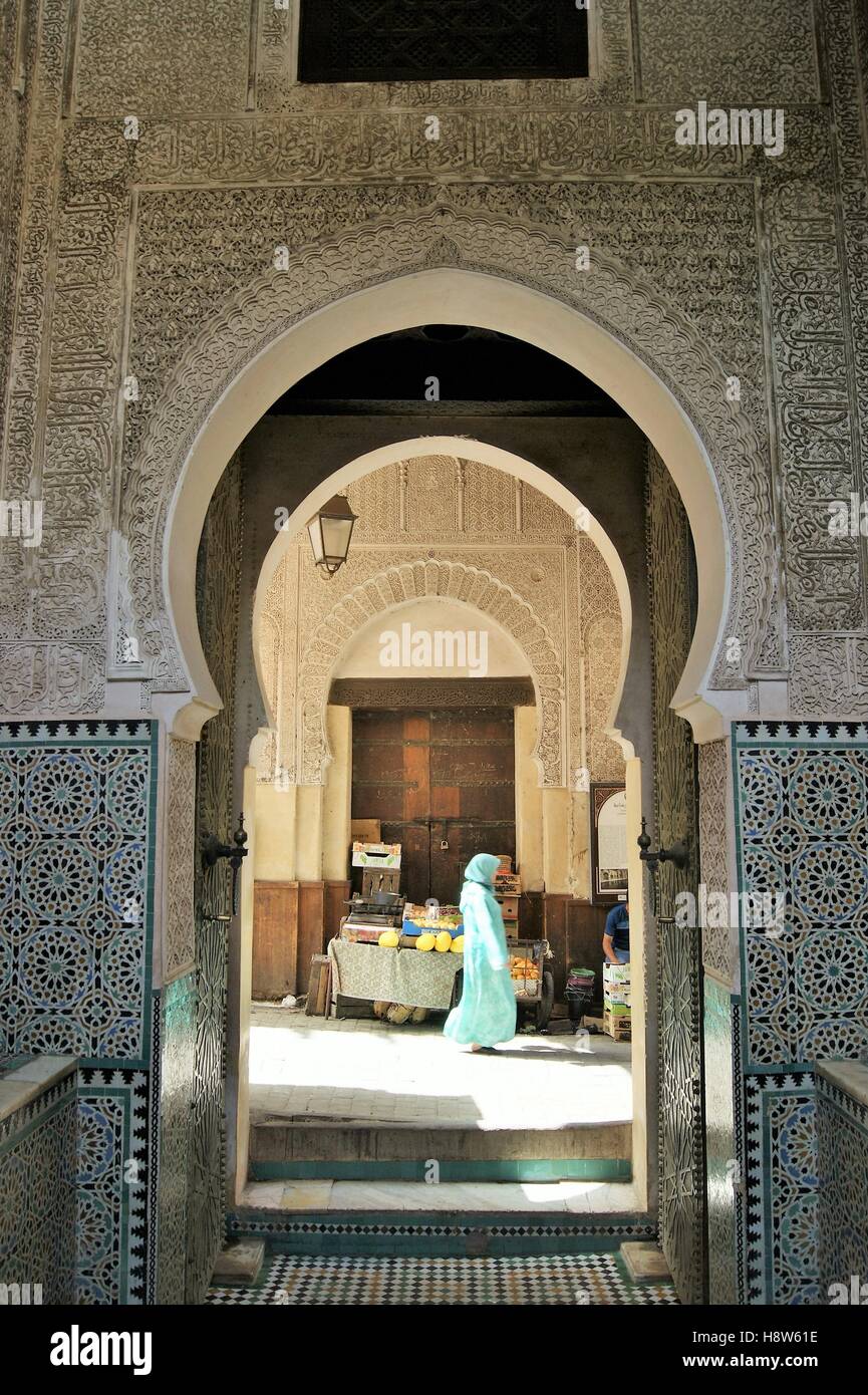 Frau geht an einer Reihe von kunstvoll gefliesten Eingängen im Fes El Bali in der alten Medina in Fez, Marokko, vorbei. Stockfoto