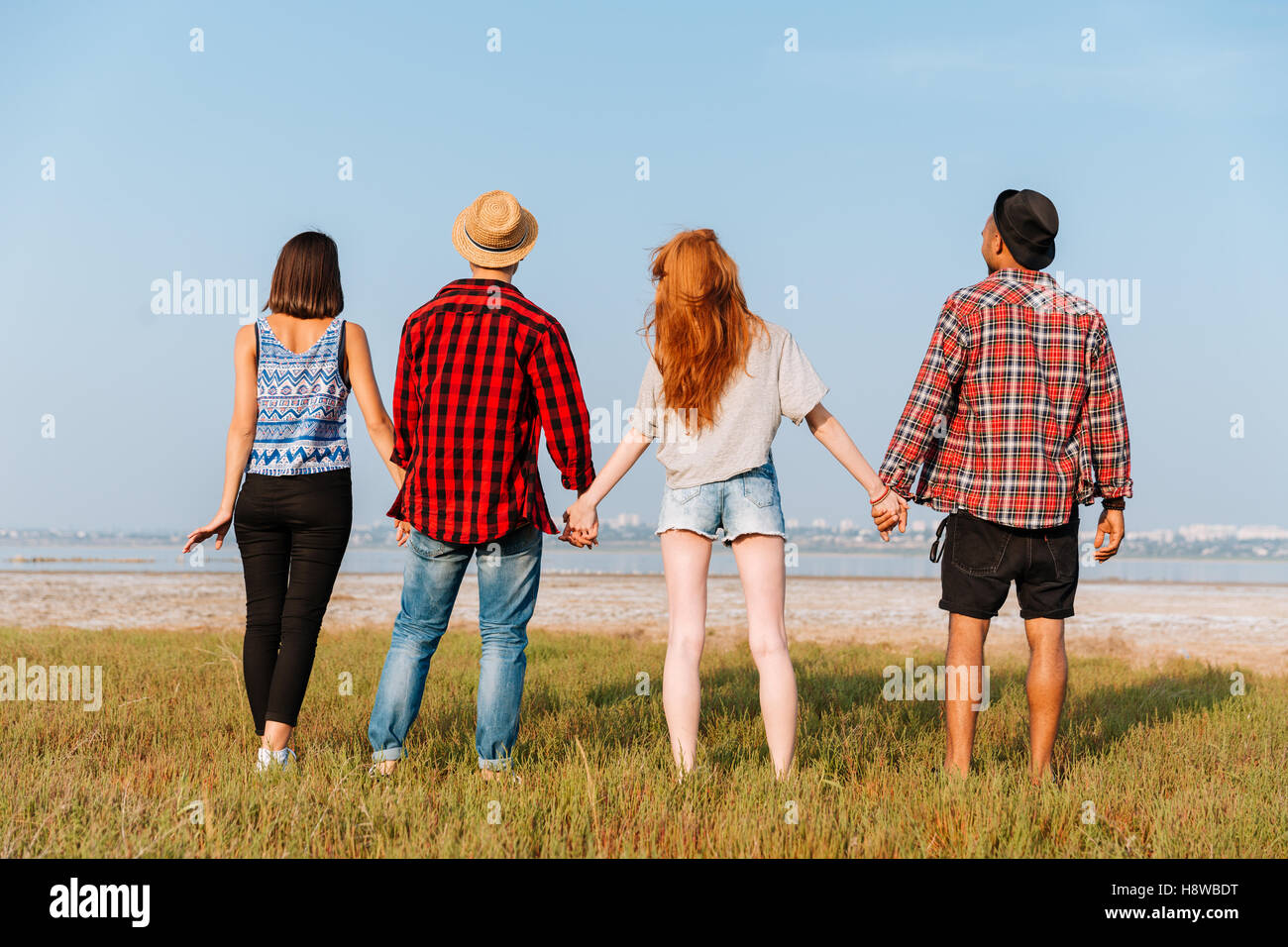 Rückseitige Ansicht vier glückliche junge Menschen stehen und Hand in Hand im freien Stockfoto