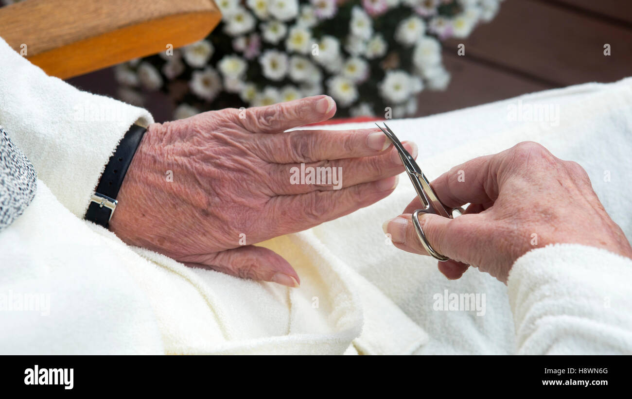 Closeup faltige alte weibliche Hände Fingernagel mit einer Schere schneiden Stockfoto