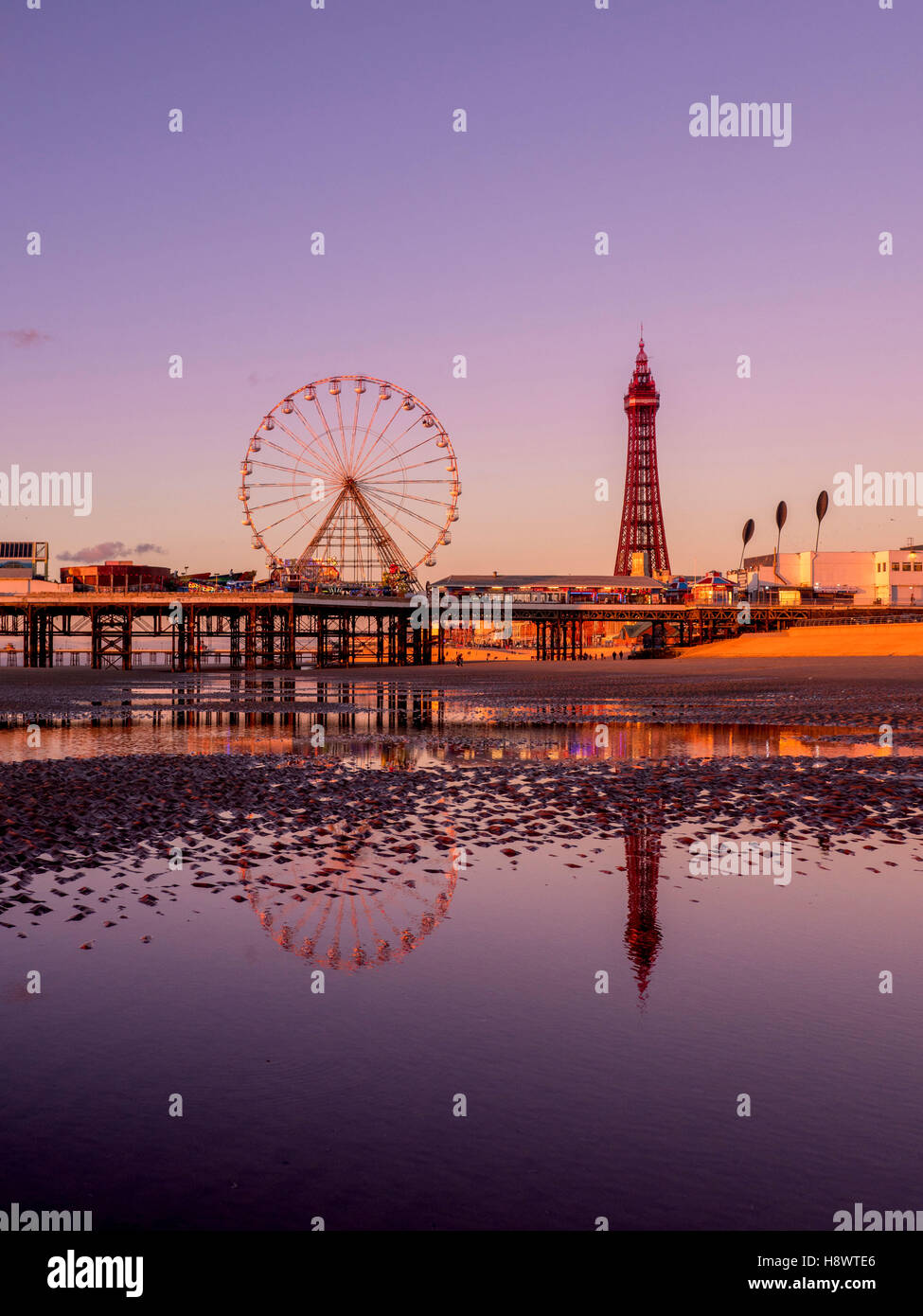 Blackpool Tower und Central Pier mit Spiegelung im Wasser am Strand bei Sonnenuntergang, Lancashire, UK. Stockfoto
