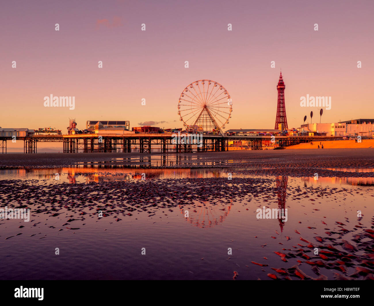 Blackpool Tower und Central Pier mit Spiegelung im Wasser am Strand bei Sonnenuntergang, Lancashire, UK. Stockfoto