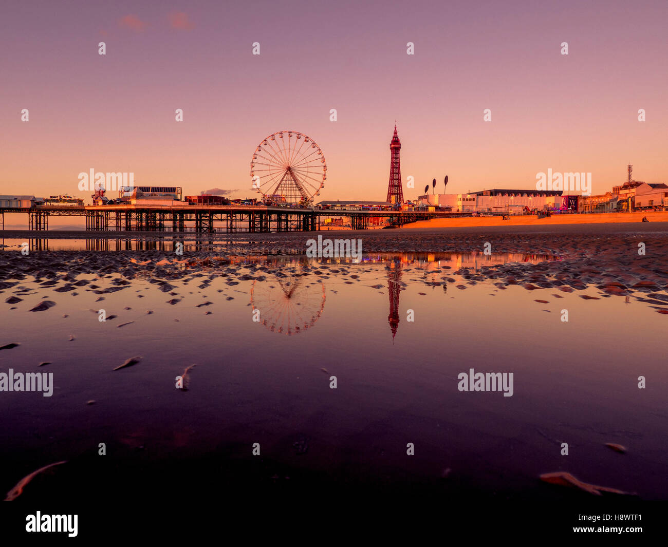 Blackpool Tower und Central Pier mit Spiegelung im Wasser am Strand bei Sonnenuntergang, Lancashire, UK. Stockfoto