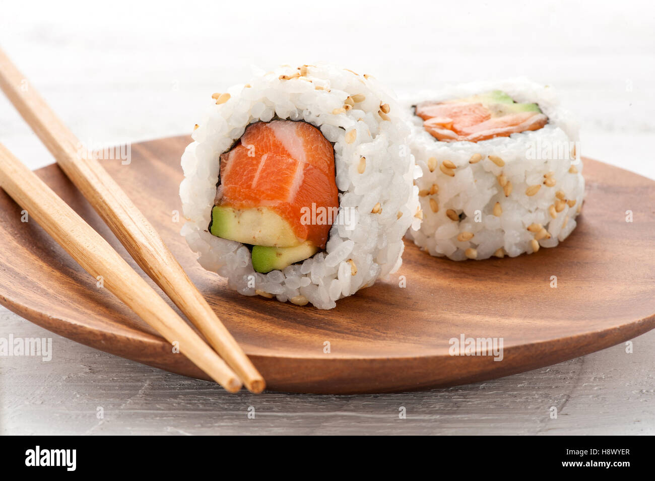 Zwei frische Lachs und Avocado Sushi Uramaki serviert auf einer Holzplatte mit einem stehend, die Zutaten zu zeigen Stockfoto