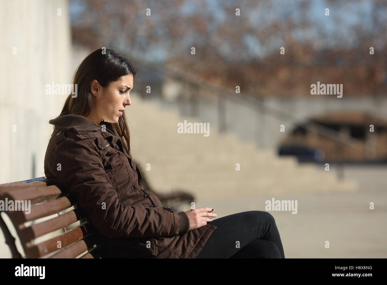 Seitenansicht einer traurig nachdenkliche Frau Rauchen sitzen in einer Bank in der Straße im winter Stockfoto