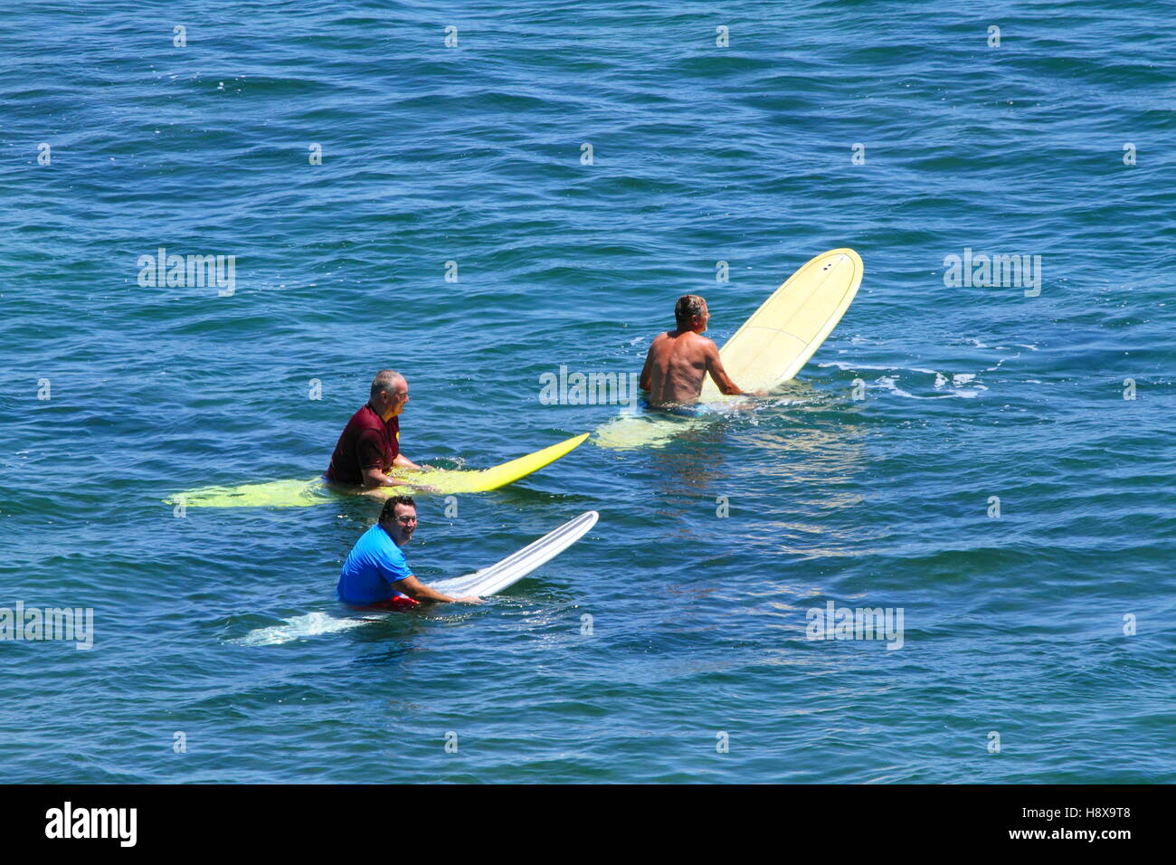 Drei ältere Menschen sitzen auf Surfbretter im Wasser beim Surfen im Moffat Beach an der Sunshine Coast in Queensland, Australien. Stockfoto