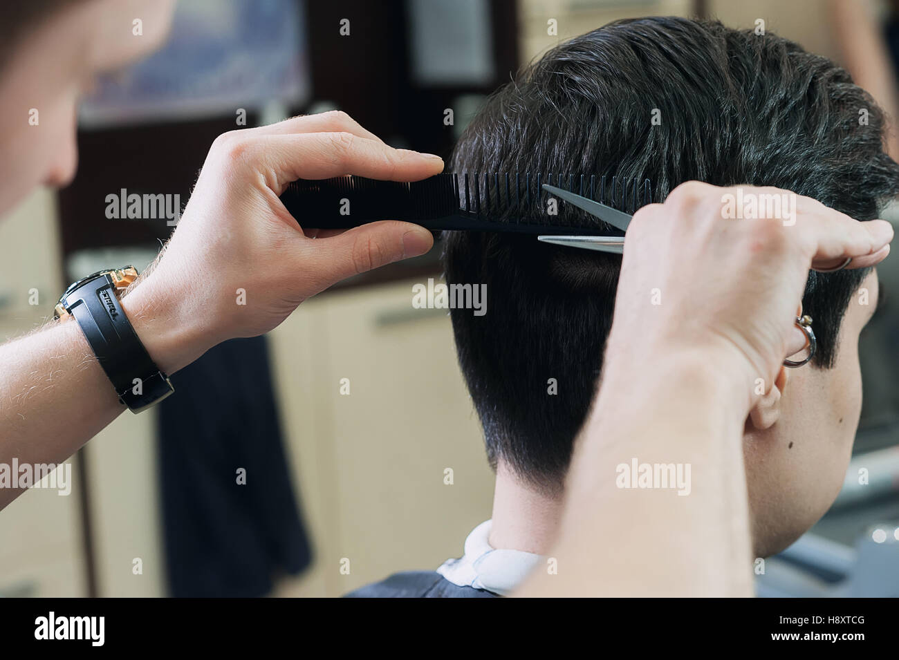 Meister Friseur schneiden einen kurzer Schnitt junger Mann im Friseurladen. dunkelhaarige Client in hellen Kap sitzen auf dem Stuhl im Barbershop. Stockfoto
