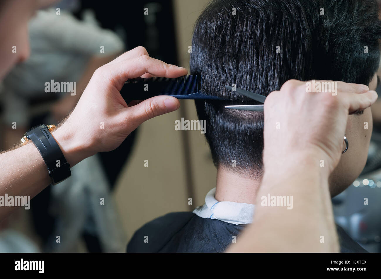 Meister Friseur schneiden einen kurzer Schnitt junger Mann im Friseurladen. dunkelhaarige Client in hellen Kap sitzen auf dem Stuhl im Barbershop. Stockfoto
