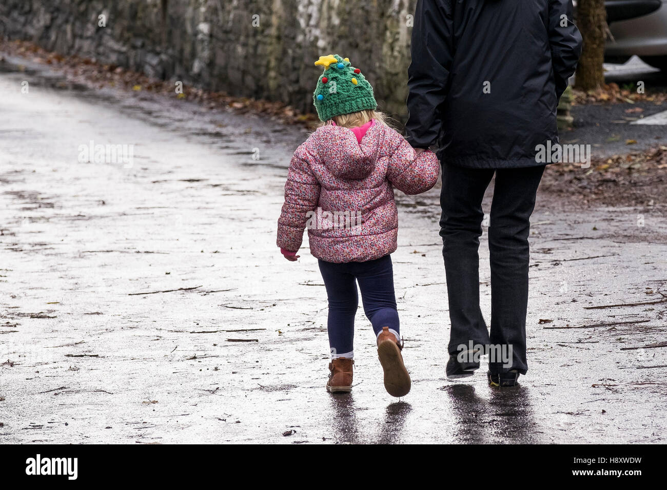 Eine Straße hinunter ein Kind und ein Erwachsener, hand in hand gehen. Stockfoto