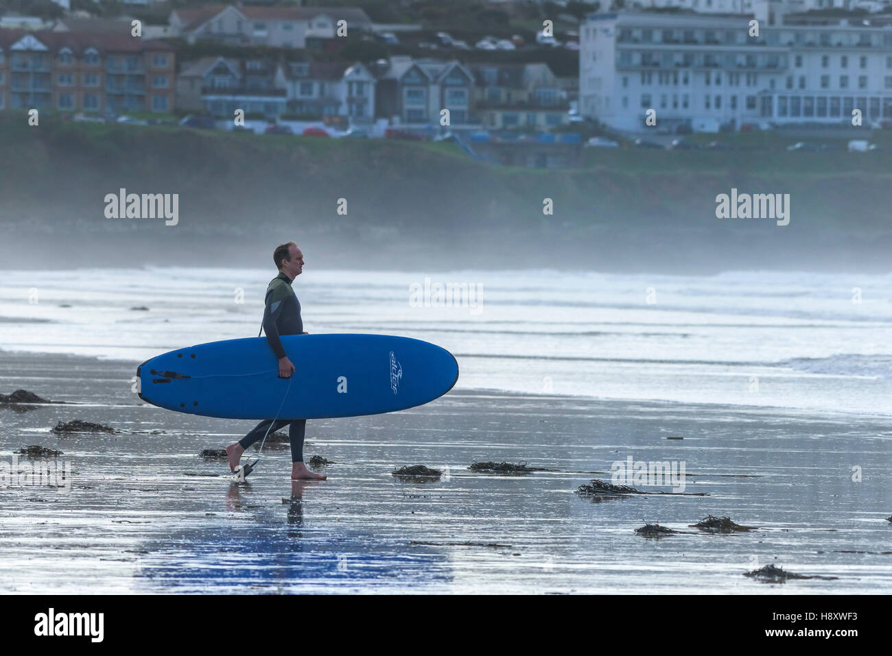 Eine Surfer trägt ein Surfbrett über den Strand am Fistral in Newquay, Cornwall. Stockfoto