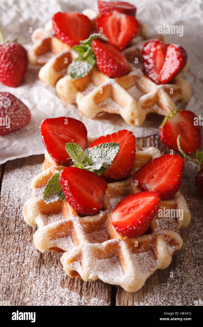 Belgische Waffeln mit Erdbeeren und Puderzucker Makro auf dem Tisch. vertikal, rustikal Stockfoto