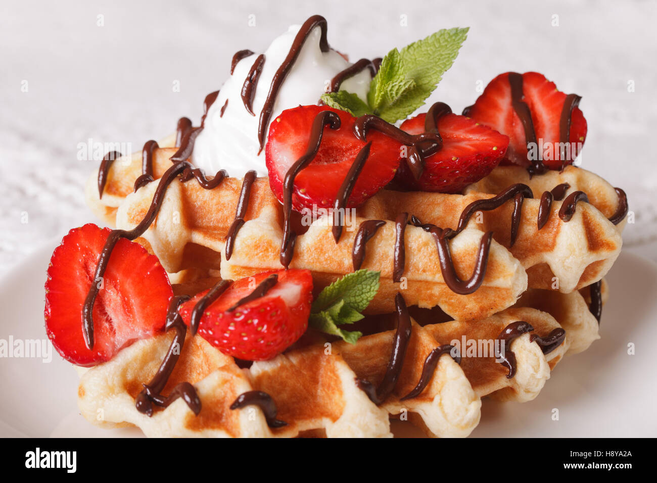 Belgische Waffeln mit Erdbeeren, Schlagsahne und Schokolade Topping Makro. Horizontale Stockfoto