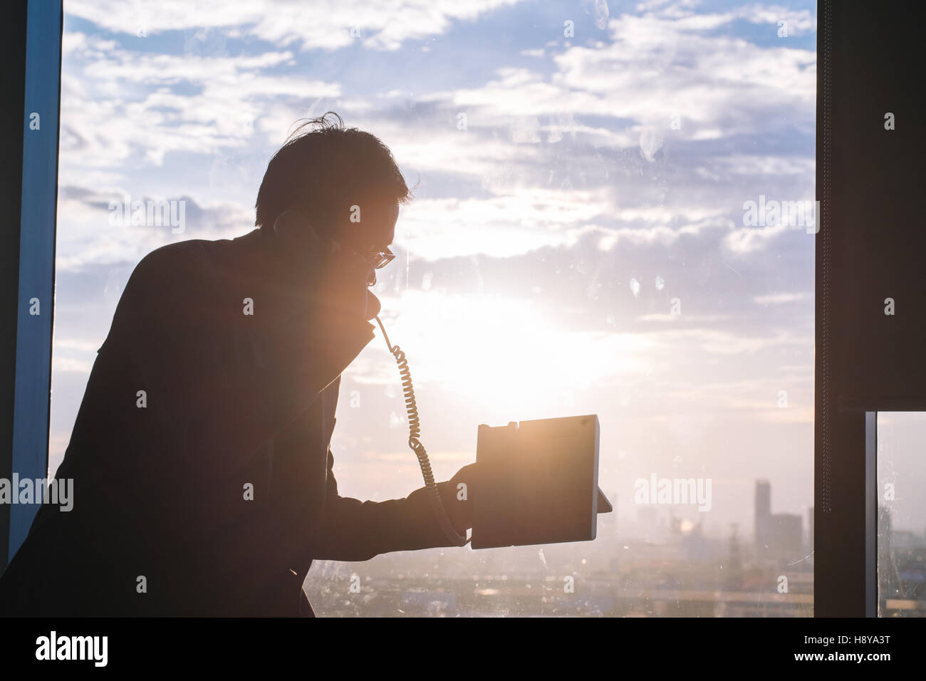 Silhouette eines Geschäftsmannes mit Telefon in Fron des Fensters im Büro Stockfoto