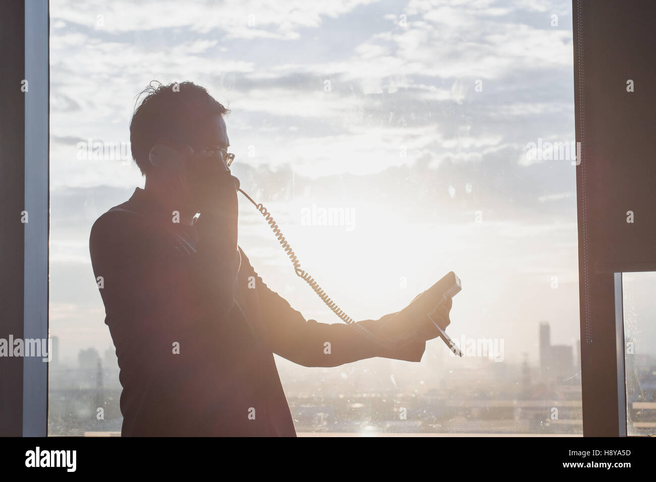 Silhouette eines Geschäftsmannes mit Telefon in Fron des Fensters im Büro Stockfoto