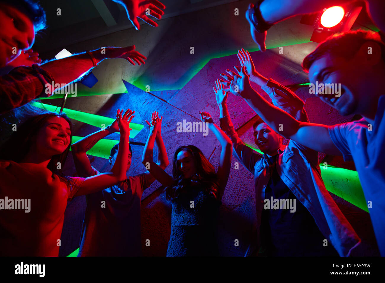 Jungs und Mädels Hände erhebend, während energetischer Tanz im Nachtclub Stockfoto