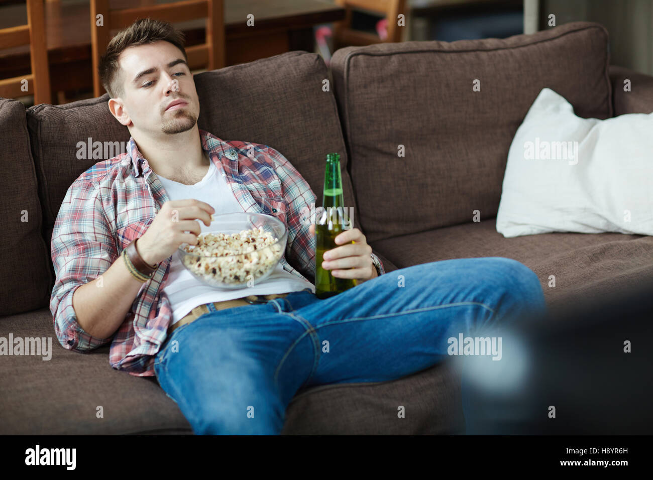 Faulen Kerl mit Schüssel Popcorn und eine Flasche Bier entspannen auf dem Sofa vor dem tv set Stockfoto