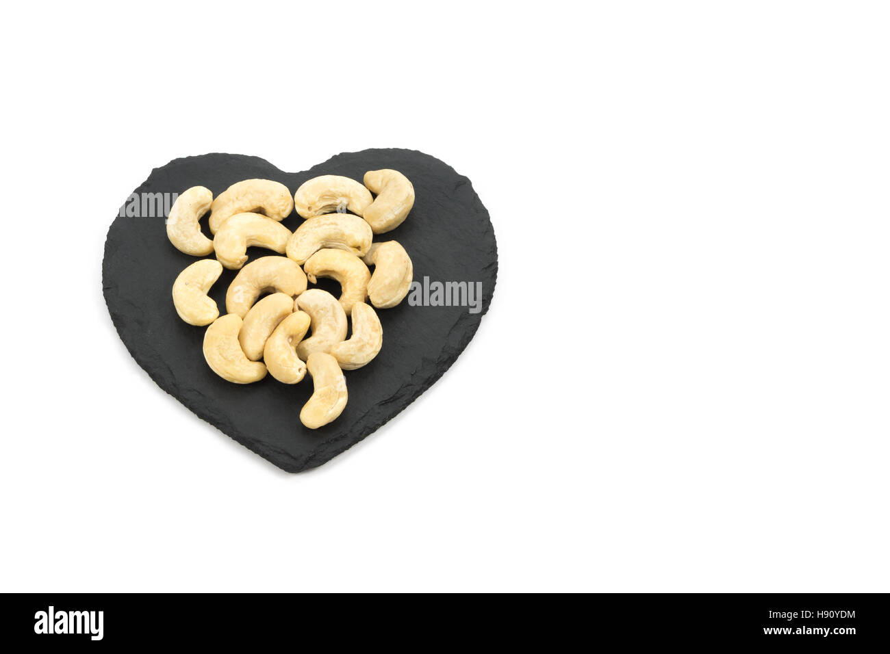 Cashew-Nüssen auf Herz geformt Schiefer isoliert auf weißem Hintergrund Stockfoto