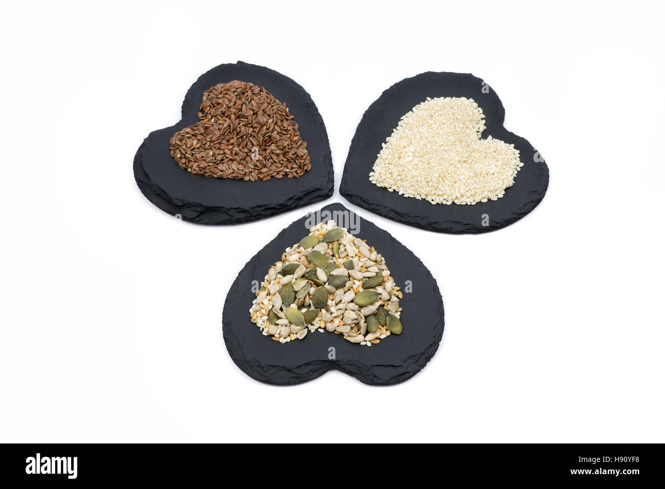 Trio von Samen, Sonnenblumenkerne, Leinsamen, Leinsamen, Kürbis und Sesam auf Herz geformt Schiefer isoliert auf weißem Hintergrund Stockfoto
