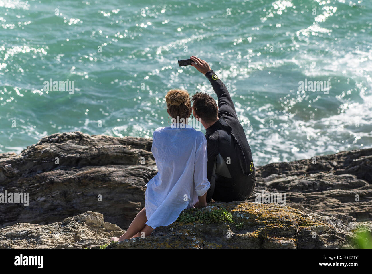 Ein paar nehmen eine Selfie, wie sie sitzen auf den Felsen am Fistral Beach in Newquay in Cornwall. Stockfoto
