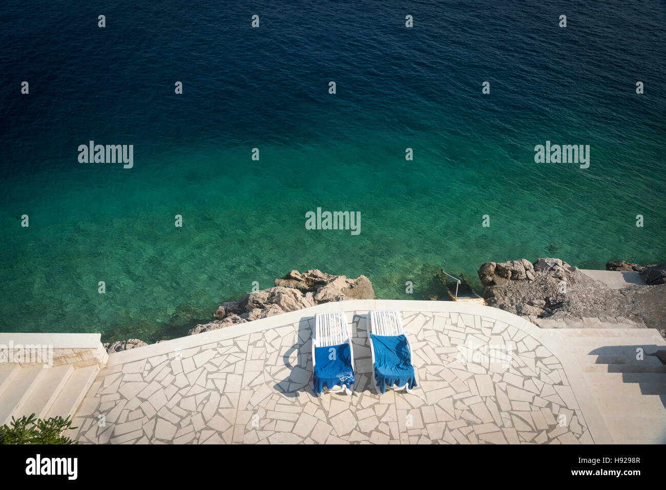 Ein Blick nach unten auf zwei Sonnenliegen auf der Terrasse von einem tiefblauen Meer in Kroatien Stockfoto