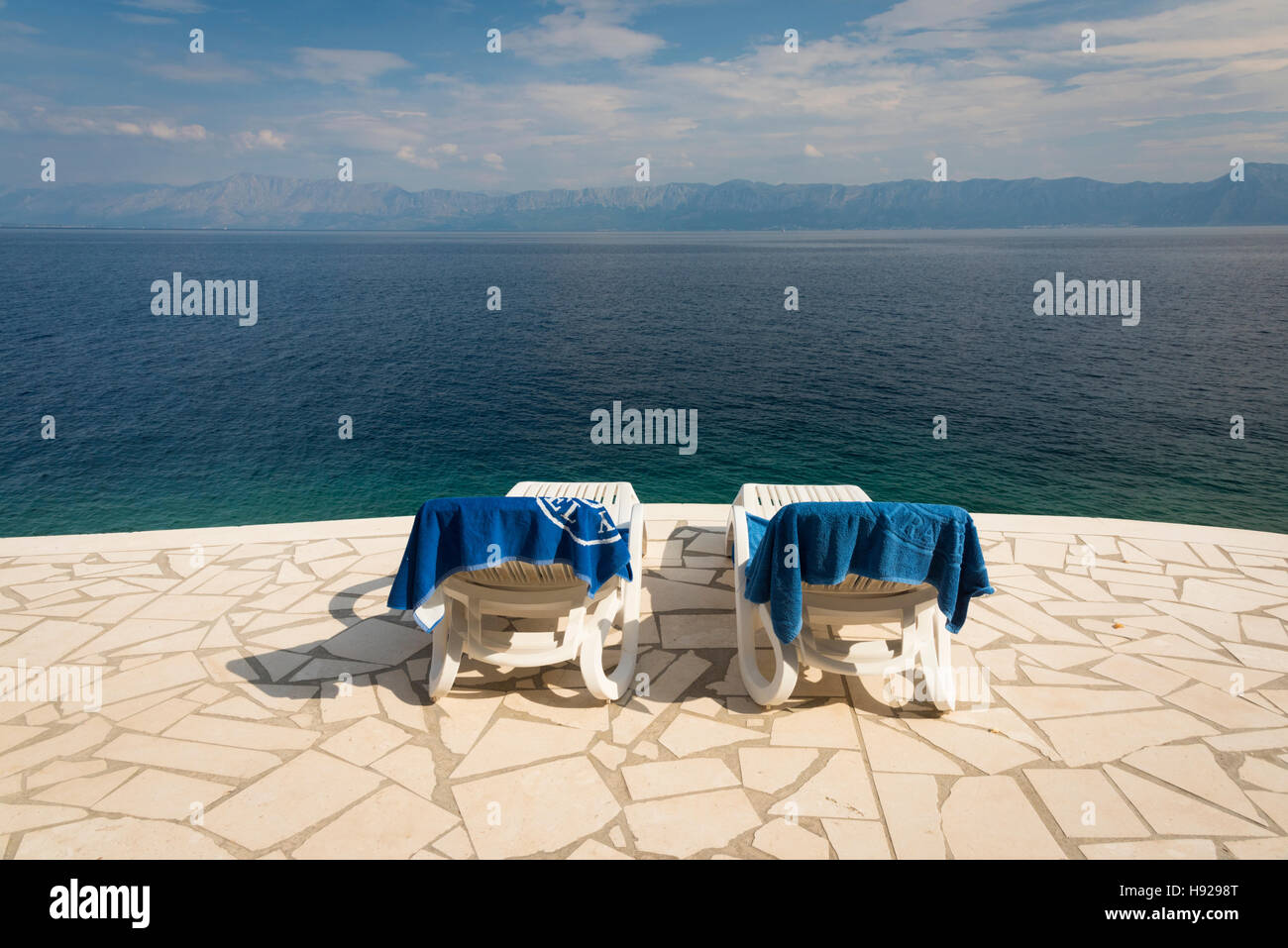 Ein Blick nach unten auf zwei Sonnenliegen auf der Terrasse von einem tiefblauen Meer in Kroatien Stockfoto