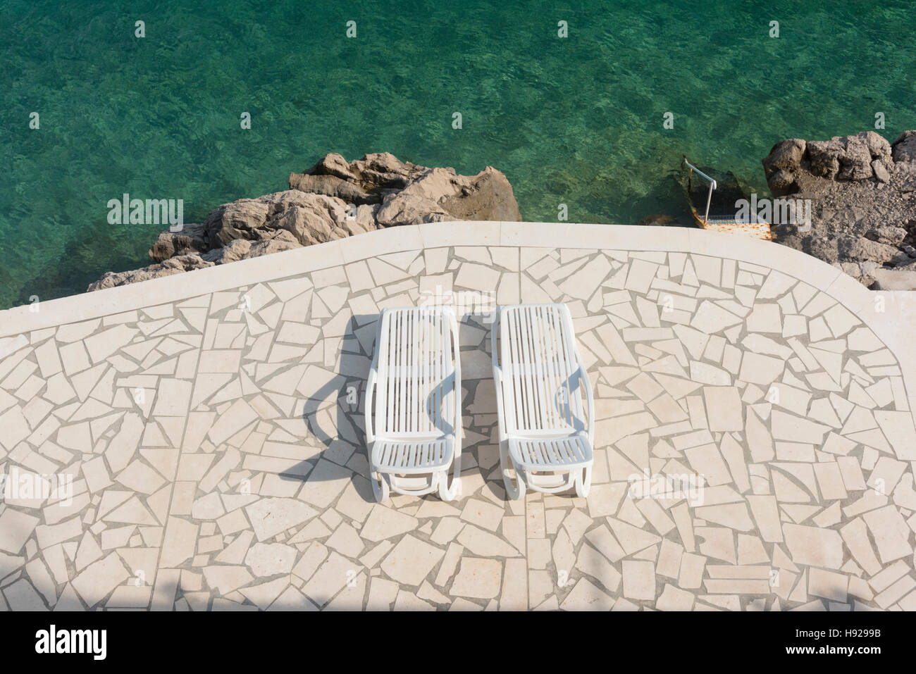 Ein Blick nach unten auf zwei Sonnenliegen auf der Terrasse von einem tiefblauen Meer in Kroatien Stockfoto