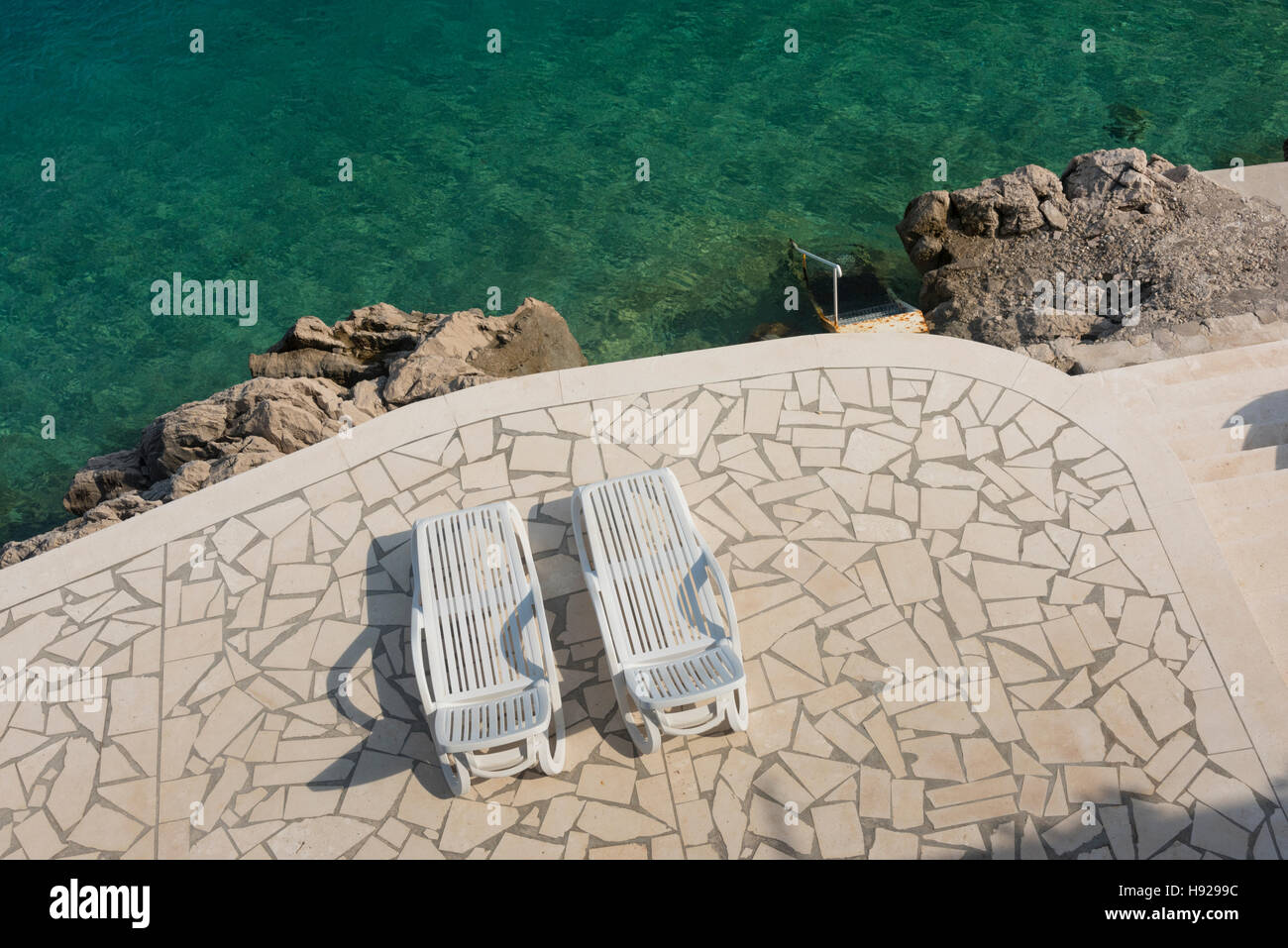 Ein Blick nach unten auf zwei Sonnenliegen auf der Terrasse von einem tiefblauen Meer in Kroatien Stockfoto