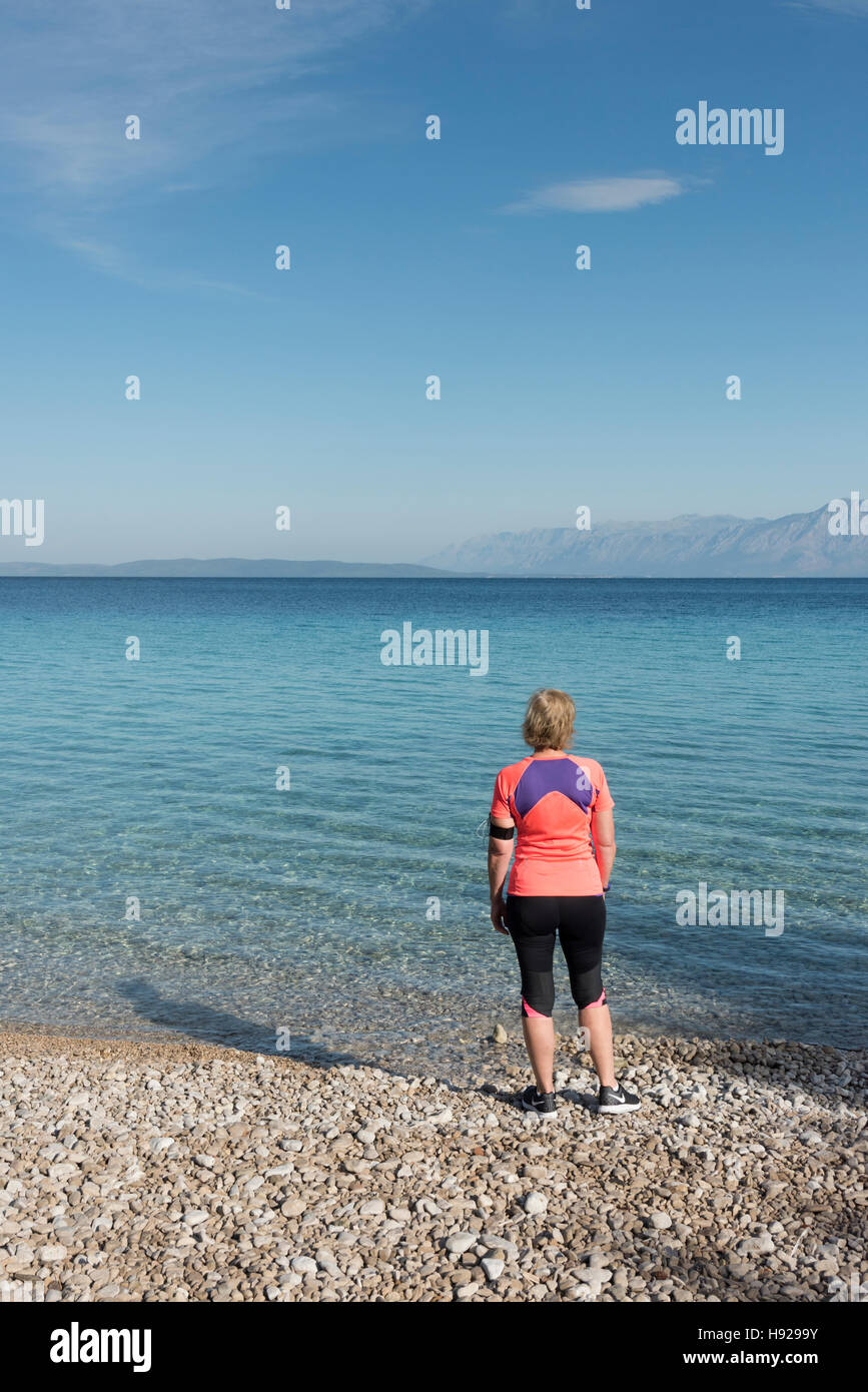 Eine Frau, gekleidet in Fahrwerk steht am Strand zurück zu Kamera Blick auf die Adria in Kroatien an einem sonnigen Tag Stockfoto