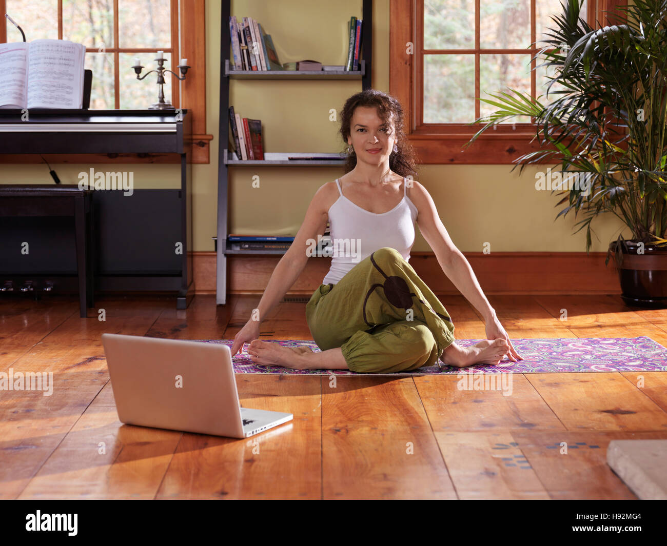 Junge Frau beim Yoga vor einem Laptop zu Hause im Wohnzimmer bei hellem Tageslicht Stockfoto
