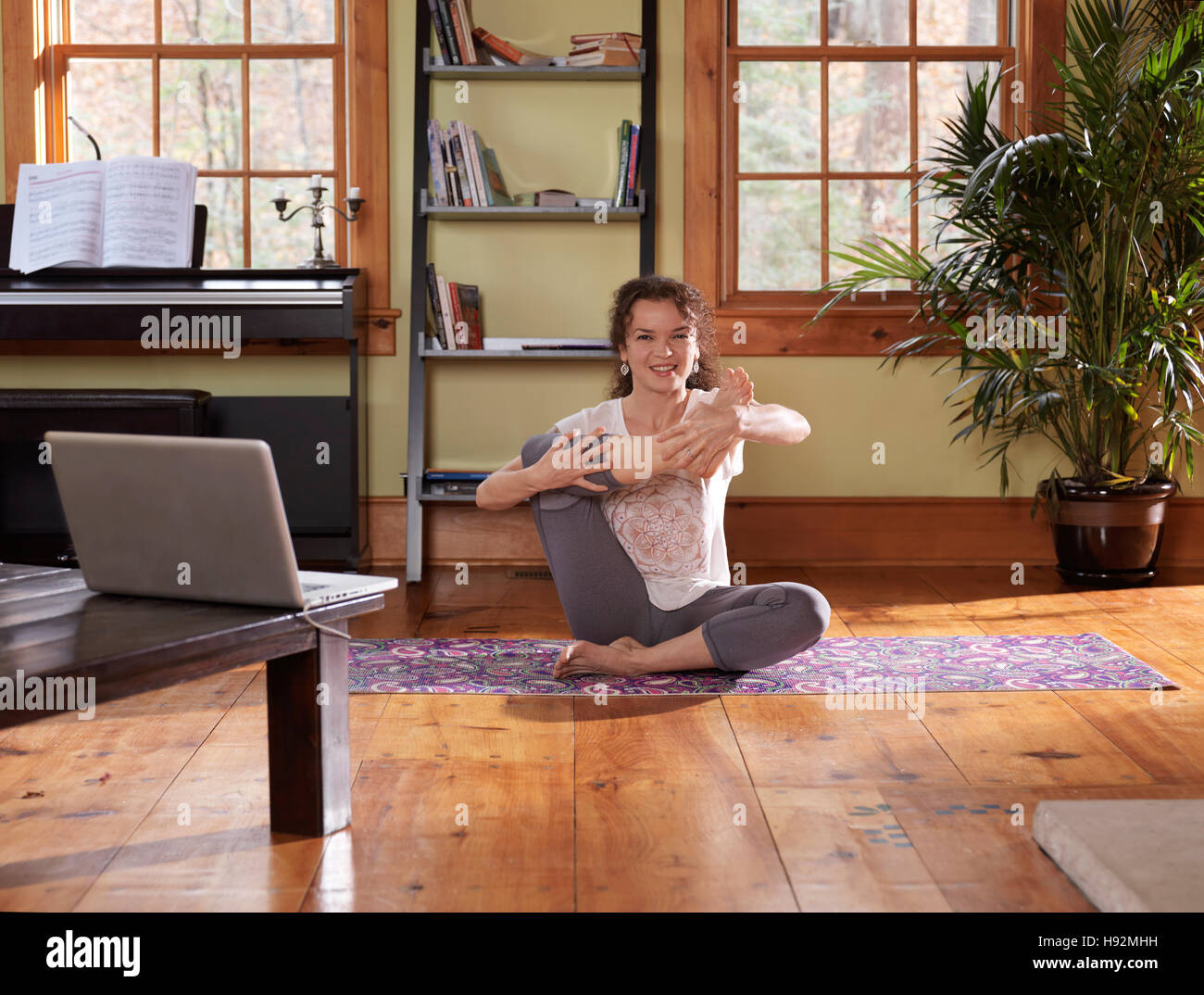 Lächelnde Frau beim Yoga vor einem Laptop zu Hause im Wohnzimmer bei hellem Tageslicht Stockfoto
