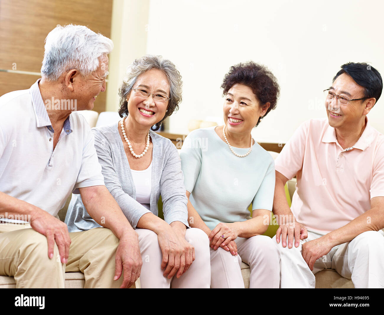 zwei glückliche und aktive senior asiatische Paare sitzen auf couch im Chat lächelnd Stockfoto
