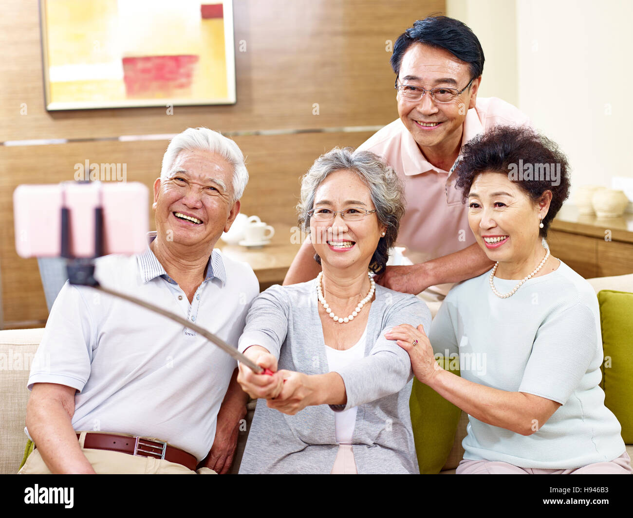 zwei aktive senior asiatische Paare nehmen ein Selbstporträt mit Handy auf einem Selfie Stick, glücklich und lächelnd Stockfoto