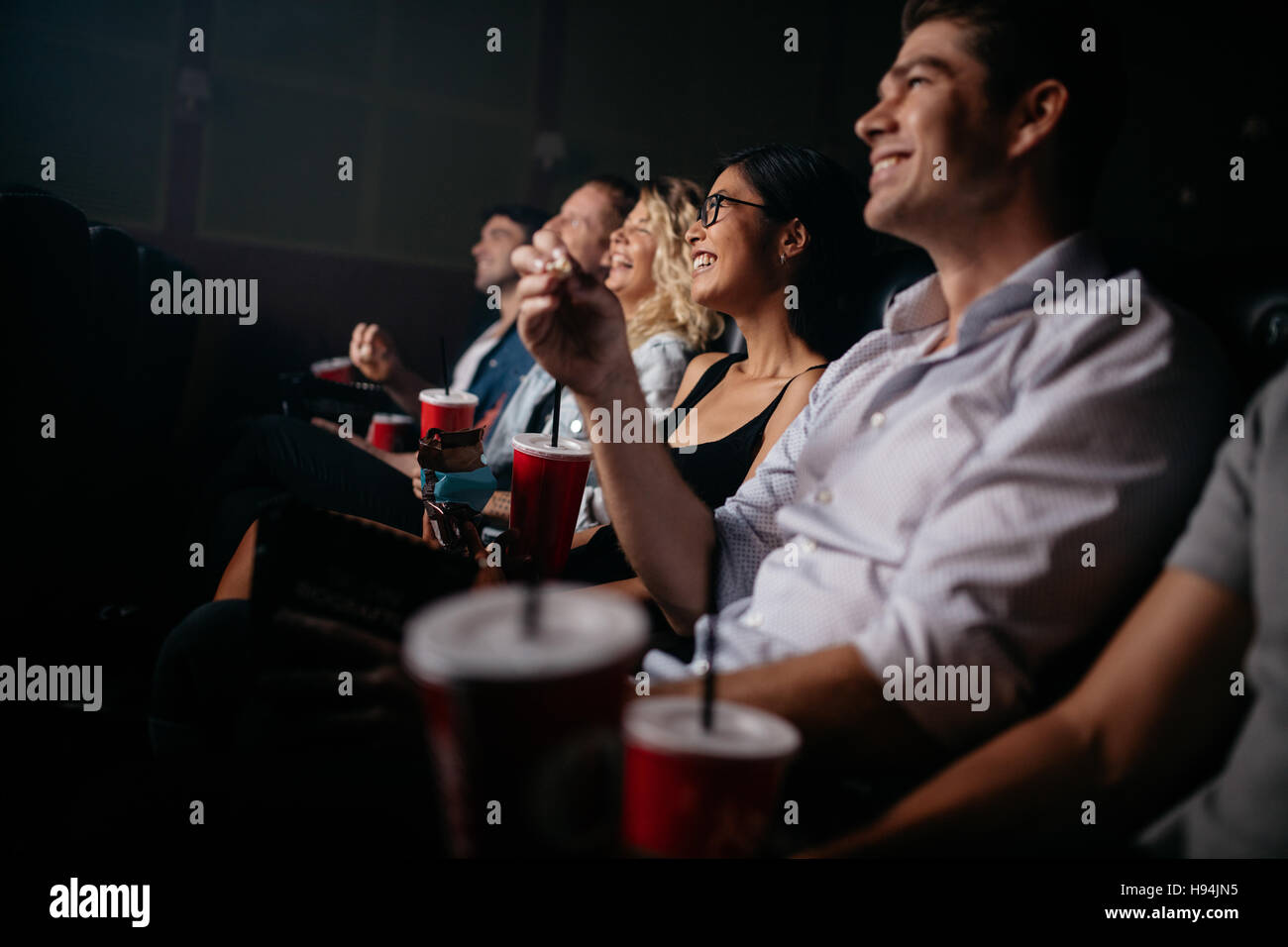 Gruppe von Personen bei Theaterbestuhlung mit Popcorn und Getränken. Junge Freunde Film im Kino. Stockfoto