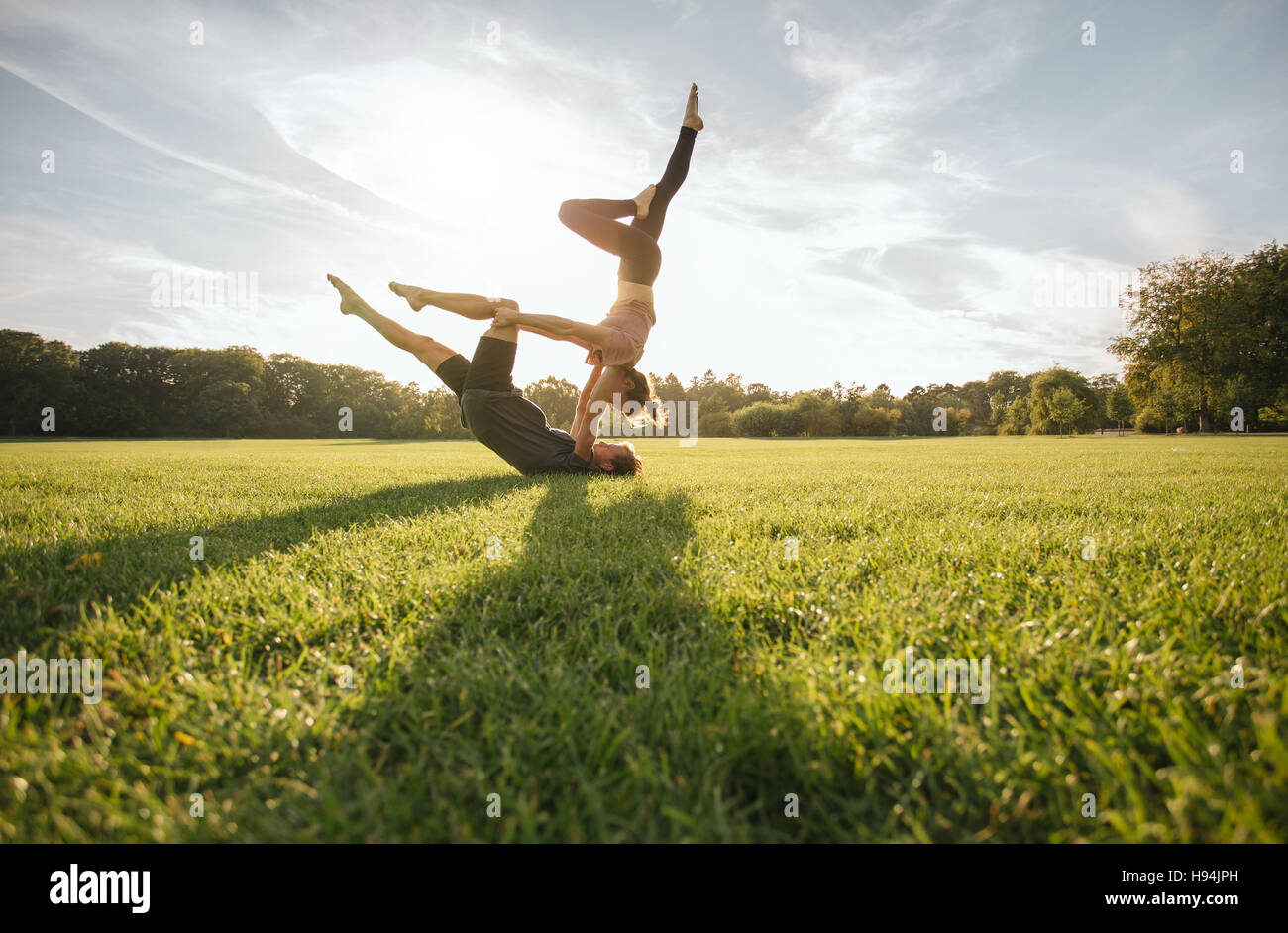 Gesunde junge Paar Acro Yoga auf dem Rasen zu tun. Mann und Frau verschiedene Yogastellungen paarweise im Freien im Park zu tun. Stockfoto