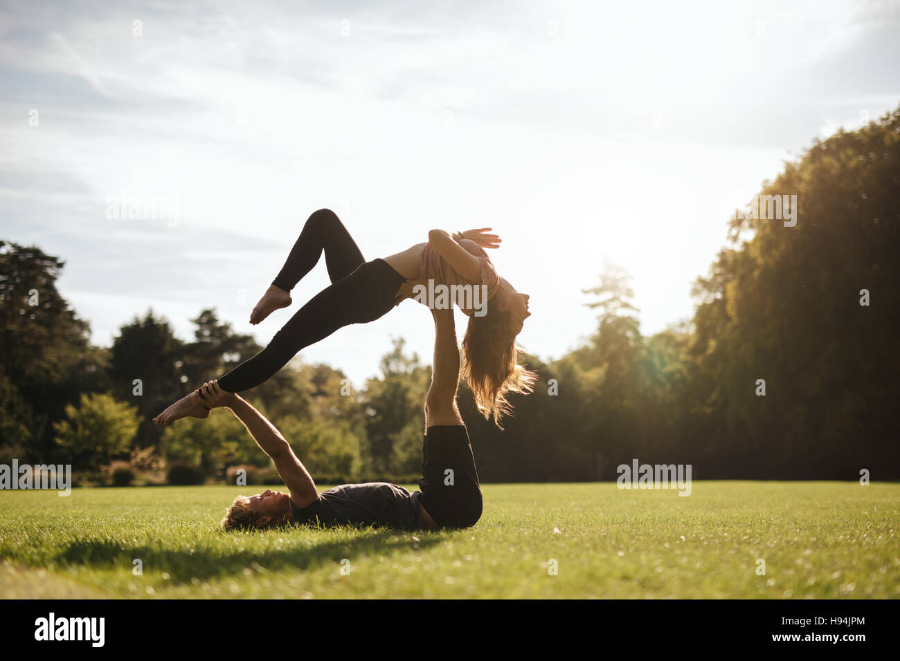 Fit paar tun akrobatische Yoga üben im Park. Mann auf dem Rasen liegen und Frau balancieren. Stockfoto