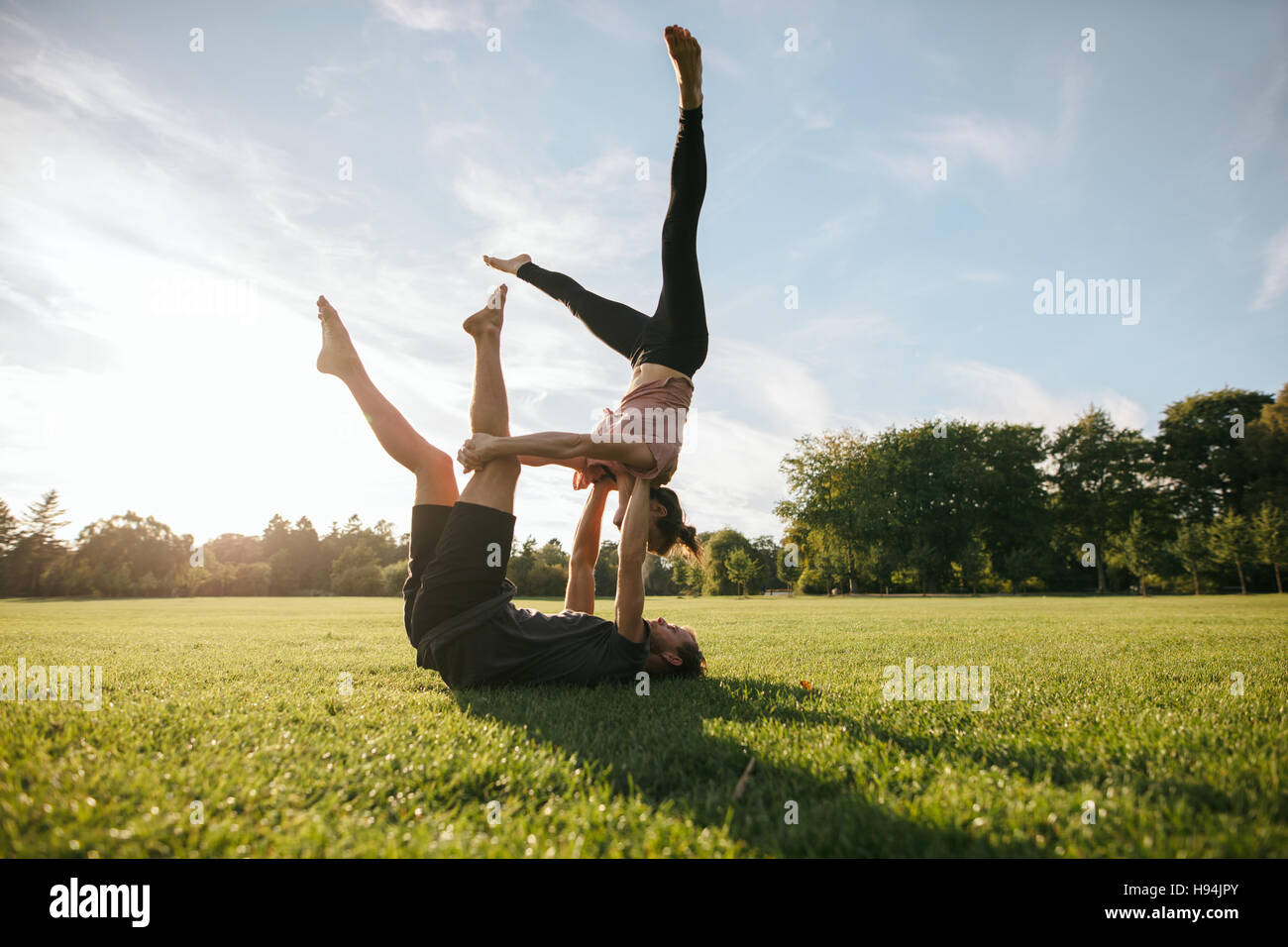 Starke und flexible junges Paar akrobatische Training zu tun. Mann und Frau im Park Morgen paar Yoga praktizieren. Stockfoto