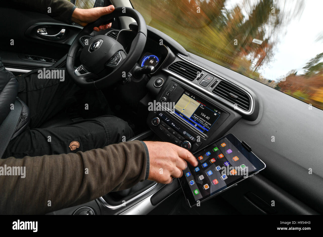 Eine Autofahrer betreibt seine iPad, die in eine integrierte Halterung während Autofahren entlang einer Landstraße in Friedrichshafen, Deutschland, 18. November 2016. Das Gesetz ist, dass jemand mit einem Mobiltelefon gefangen während der Fahrt ist erforderlich, um eine Geldstrafe zu zahlen. Aber bisher das Schreiben einer SMS oder die Verwendung eines Tablet-PCs nicht ausdrücklich in der Straßenverkehrsordnung und der Bundesminister für Verkehr verboten ist jetzt will das ändern. Foto: FELIX KAESTLE/DPA Stockfoto