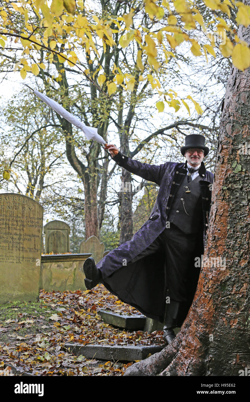 Haworth, Vereinigtes Königreich. 19. November 2016. Ein Mann, gekleidet in ein Steampunk entworfen Kap ungeöffneten Regenschirm, lehnte sich gegen einen Baum auf dem Friedhof, Haworth, 19. November 2016 halten. Bildnachweis: Barbara Koch/Alamy Live-Nachrichten Stockfoto