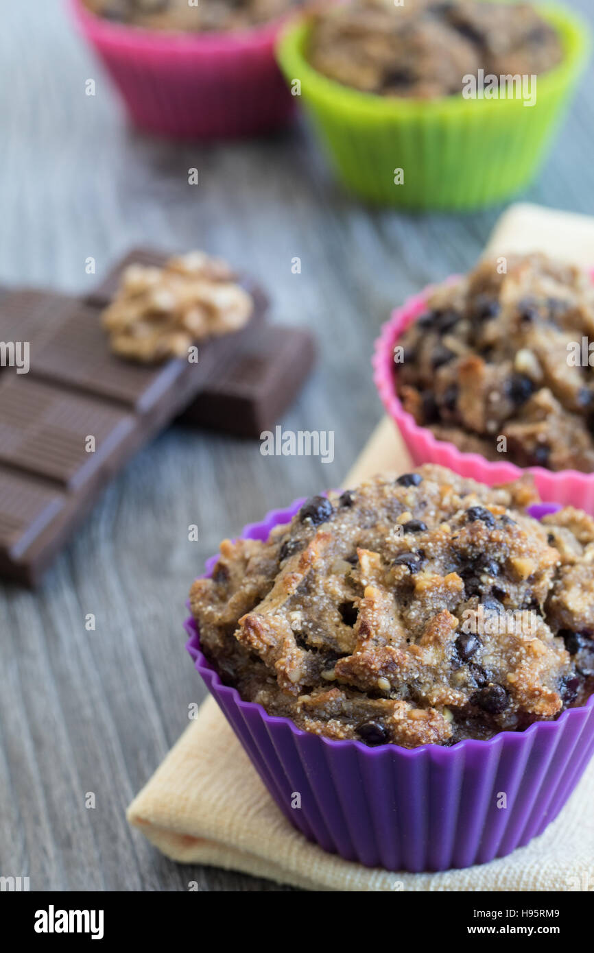 Obst-Muffins auf einem gelben Serviette und einem grauen Holztisch. Walnüsse, Schokolade und zwei aus Fokus Muffins im Hintergrund. Stockfoto