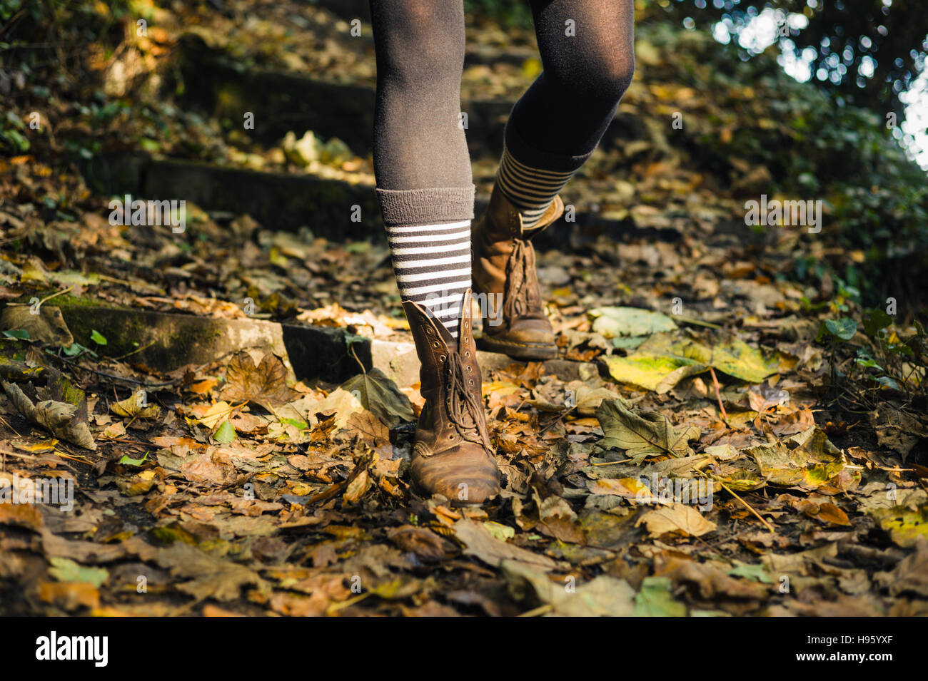 Die Beine einer jungen Frau mit gestreiften Socken und Stiefel, wie sie Fuß in einem Wald im Herbst Stockfoto